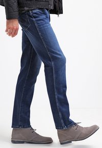 Blå denimjeans med rak passform, med en subtil tvätt och sidostygn, i kombination med grå mocka ankelskor.