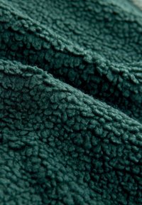 Tume rohelise kangaga, millel on tekstuuriga, pehme pind. Materjal näib olevat pehme ja karvane, lainelise mustriga kõrgendatud muhketega üle kogu pinna.