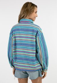 Giacca oversize multicolore con modelli geometrici in blu, rosa, verde e oro. Realizzata in un tessuto texturizzato con colletto.