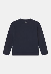 Marinblå bomullströja, rundad halsringning, långa ärmar, ribbade muddars och nederkant. Har en liten grön logotyp vid bakre halsringningen.