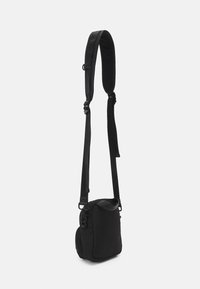 Sort crossbody taske med polstret rem, rektangulær form, slidstærkt stof, lynlås lukning og en accentpanel på klaffen.