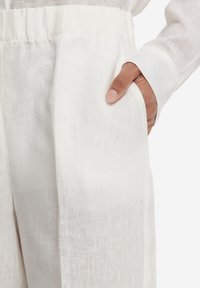 Hvide linnedbukser med elastisk taljebånd, sidelommer og et let, tekstureret stof. Designet lægger vægt på enkelhed og komfort.