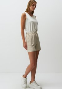 Lichte beige shorts met een elastische tailleband en trekkoord, gecombineerd met een aansluitend wit tanktop en witte sneakers. Glad stof.