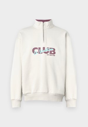 Heled kreemisa sweatshirt kõrge kraega ja pool tõmblukuga. Omab lilla ja teal värvi graafilist printi: "CLUB Puhkusel LÄHEME REISILE."