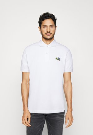 Camisa polo blanca con tapeta de tres botones, mangas cortas y un pequeño logo bordado de cocodrilo verde en el lado izquierdo del pecho.