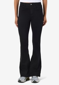 Calças pretas flare com cintura justa, cinco bolsos e detalhes sutis de costura, combinadas com ténis desportivos cinzentos.