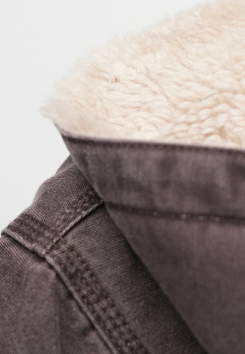 Brown jacket collar with soft, beige faux fur lining; visible stitching and textured fabric detail on the exterior.