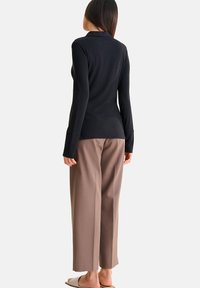 Zwart geribbelde blouse met lange mouwen in combinatie met beige wijde pantalon. De blouse heeft een getailleerde snit en een klassiek kraagontwerp.