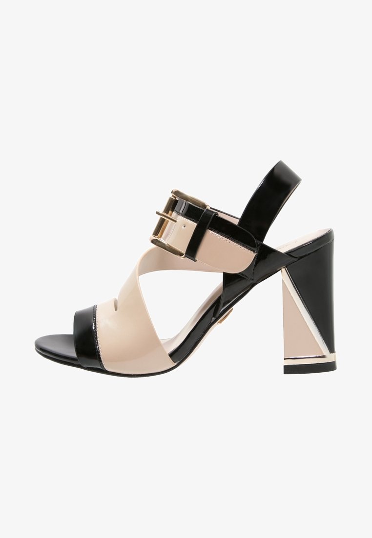 Sandale noire et nude à lanières avec un talon bloc, présentant une finition brillante en vernis, un détail de boucle dorée et un accent de talon géométrique.