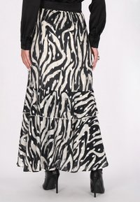 Maxirock in Schwarz und Creme mit einem wellenförmigen Streifenmuster und Punkten. Verfügt über ein gestuftes Design und einen elastischen Bund. Kombiniert mit High Heels.