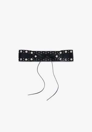 Cintura in pelle nera con grandi borchie circolari in argento, caratterizzata da un dettaglio a fiocco annodato al centro. Texture liscia, forma piatta e rettangolare.