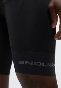 Μαύρο ποδηλατικό σορτς στον μηρό ενός ατόμου με το όνομα της μάρκας "ENDURA" σε αντανακλαστικά γράμματα κοντά στο τελείωμα.