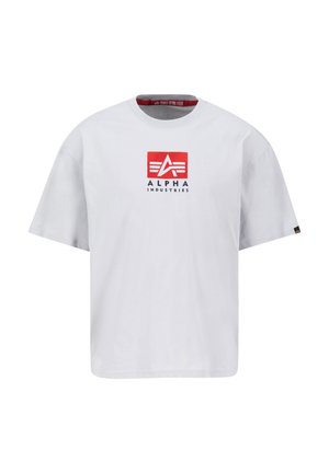 Fehér pamut póló kerek nyakkal, elöl piros négyzet alakú logóval, amelyen fehér és fekete szöveg olvasható: "ALPHA INDUSTRIES". Rövid ujjú.