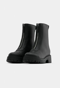 Μαύρες δερμάτινες μπότες μέχρι τον αστράγαλο με φερμουάρ μπροστά, χοντρή σόλα και υφή στην επιφάνεια. Διαθέτουν λεία επιφάνεια και κομψό, μινιμαλιστικό σχέδιο.