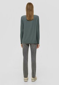 Lange mouw, mintgroene top met een ronde hals, gecombineerd met grijze, rechte broek en creamkleurige sneakers. Glad ontwerp, casual stijl.