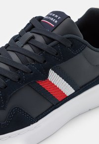 Granatowe trampki z połączenia gładkiej skóry i zamszu, z czerwonymi i białymi poziomymi paskami oraz białą gumową podeszwą.