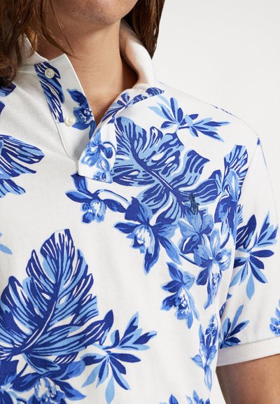 Λευκό πόλο πουκάμισο με μπλε ανθικά και φυλλώδη μοτίβα. Διαθέτει γιακά με κουμπιά και υφασμάτινη υφή. Λεπτή κεντ�ημένη λεπτομέρεια λογότυπου.