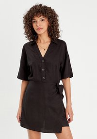 Schwarzes Leinenkleid mit V-Ausschnitt, kurzen Ärmeln, Knopfverschluss und seitlichem Bindedetail, mit einer lässigen Silhouette und weicher Textur.