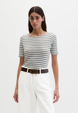 Femme portant un t-shirt à manches courtes rayé gris et blanc, un pantalon blanc, et une ceinture marron foncé avec une boucle dorée.
