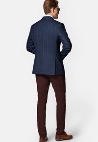 Marynarski blazer w kratę z brązowymi akcentami, zestawiony z ciemno-brązowymi chinosami. Gładka tekstura, dopasowany krój i brązowe skórzane buty.