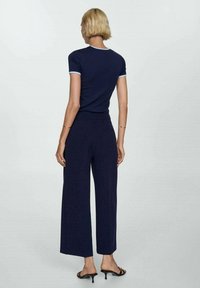 Haut à manches courtes bleu marine avec des bordures bleu clair associé à un pantalon large bleu marine. L'ensemble est confectionné dans un tissu lisse et extensible.