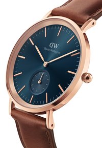 Orologio rotondo con quadrante blu navy, dettagli in oro rosa, un subquadrante e cinturino in pelle marrone. Caratterizzato da marcatori delle ore allungati e corona.