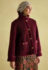 Burgundia värvi fliisjakk kõrge kraega, kuldsete nuppudega ja kahe esipocketiga. Pehme tekstuur luksusliku viimistlusega ja triibulised varrukaaktsentidega.