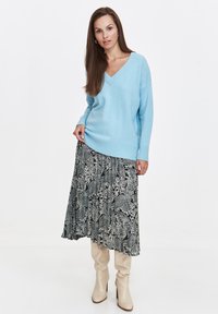 Jasnoniebieski sweter dziany z dekoltem w serek, w połączeniu z czarną i białą spódnicą w paisley oraz beżowymi botkami do kolan.