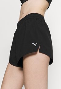 Svarta träningsshorts i lätt material, med hög midja, sidoflikar och en liten vit Puma-logotyp på fållen.