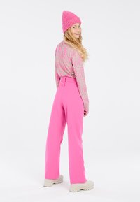Un pantalon long rose à taille haute, associé à un haut à manches longues à motifs en rose doux et beige, et un bonnet texturé rose assorti.