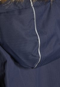 Mørkeblå jakke med herringbone tekstur, med en grå detalj på sømmen, og en avtakbar pelsdetalj på hetten.