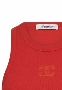 Rdeča rebrasta brezrokavnik z okroglim izrezom in izvezenim logotipom s prekrivašimi črkami v središču. Oznaka navaja "co'couture."
