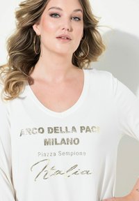Weißes V-Ausschnitt-Shirt mit metallic-goldener Schrift: "ARCO DELLA PACE MILANO Piazza Sempione Italia." Lange Ärmel mit glatter Textur.