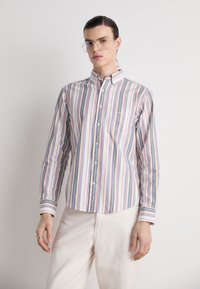 Camisa de botones a rayas con rayas azules, rojas y amarillas sobre un fondo blanco, con un bolsillo en el pecho y cuello clásico.