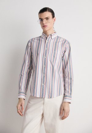 Chemise à rayures avec des rayures bleues, rouges et jaunes sur fond blanc, dotée d'une poche poitrine et d'un col classique.