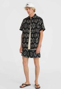 Short-sleeve black shirt with geometric patterns in cream and teal, paired with matching shorts. Both are made of lightweight fabric.