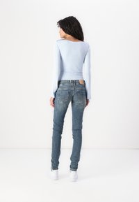 Light blue long-sleeve top paired with faded blue slim-fit jeans. The outfit features a simple design and minimal detailing. White sneakers.