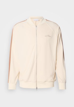 Giubbotto bomber crema con chiusura a zip, righe marroni a contrasto sulle spalle, polsini a costine e discreta ricamata sul petto.