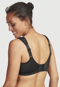 Mustaa rintaliivit säädettävillä olkaimilla, hakasella kiinnitys ja teksturoidut ompeleet. Omaavat sileän kangaspinnan.