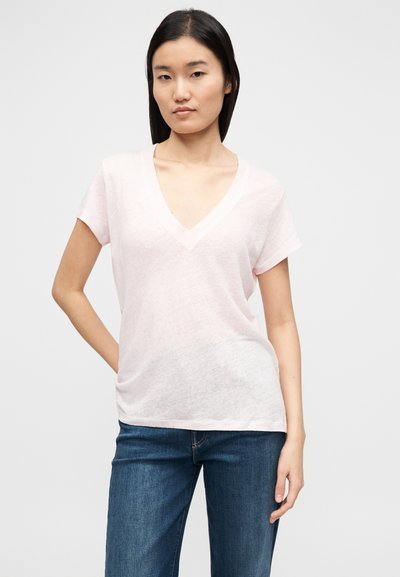 Tricou roz deschis cu decolteu în V și mâneci scurte, realizat dintr-un material moale, texturat. Purtat cu blugi albaștri, având o croială lejeră.