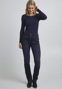Námořnické tričko s dlouhým rukávem a scalloped výstřihem v kombinaci s tmavě modrými slim-fit džíny. Texturovaná látka, jemné detaily a uzávěr na dva knoflíky.