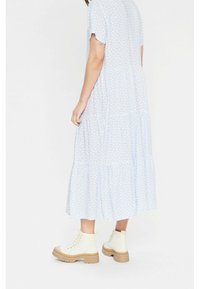 Himmelblaues gestuftes Kleid mit weißem Herzmuster, kurzen Ärmeln und lockerer Passform, kombiniert mit cremefarbenen Stiefeln mit dicker Sohle.