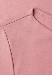 Světle růžový svetr s crew neck, vyrobený z hladké, texturované látky, s švy na ramenním švu a výstřihu.