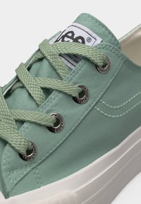 Πανίνο αθλητικό παπούτσι σε μέντα πράσινο με χοντρές κορδόνια σε ανοιχτό πράσινο, λευκή λαστιχένια σόλα, μεταλλικές τρύπες κορδονιών με τη σήμανση "Lee 1889" και ραμμένη λεπτομέρεια στο πλάι.