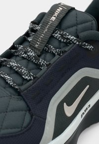 Sneaker Nike z ciemnoniebieską pikowaną cholewką, teksturowanym materiałem, kontrastującymi czarnymi i szarymi sznurowadłami oraz srebrnym logo Swoosh z boku.