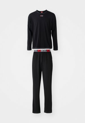 Juodas ilgomis rankovėmis megztinis ir suderintos kelnės, pagamintos iš minkštos medžiagos. Megztinis turi raudoną akcentuotą logotipą ir raštuotą liemenį.