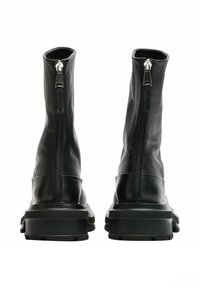 Stivali alla caviglia in pelle nera con un design elegante, tarsi alti e cerniere laterali ben visibili; suole nere spesse con grip testurizzati.