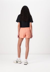 Black ribbed t-shirt, soft peach shorts with a textured finish, elastic waistband, and white sneakers with green accents.