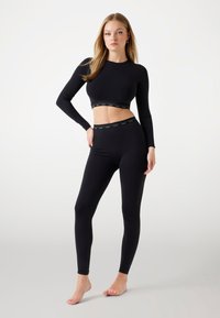 Top corto negro de manga larga con un diseño ajustado y una banda elástica de marca. Leggings negros a juego con una banda elástica similar en la cintura.