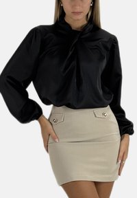 Schwarze Satinbluse mit Puffärmeln und verdrehtem Ausschnitt, kombiniert mit einem beigen Minirock mit dekorativen goldenen Knöpfen.